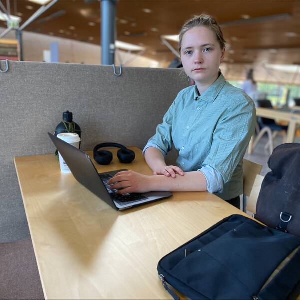 En bild på en student, James Jonsson, i en grönblå skjorta som sitter framför en dator.