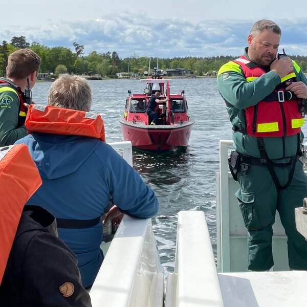 Flera personer iklädda flytväst syns i bild ombord på en båt. På båten finns också två män iklädda ambulansuniformer. En röd räddningstjänsbåt närmar sig.