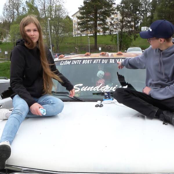 Två ungdomar – en tjej och en kille – sitter på en vit motorhuv. Killen pekar på dekalen i ovankanten på vindrutan, det står ”Kom ihåg att du är värdefull”.