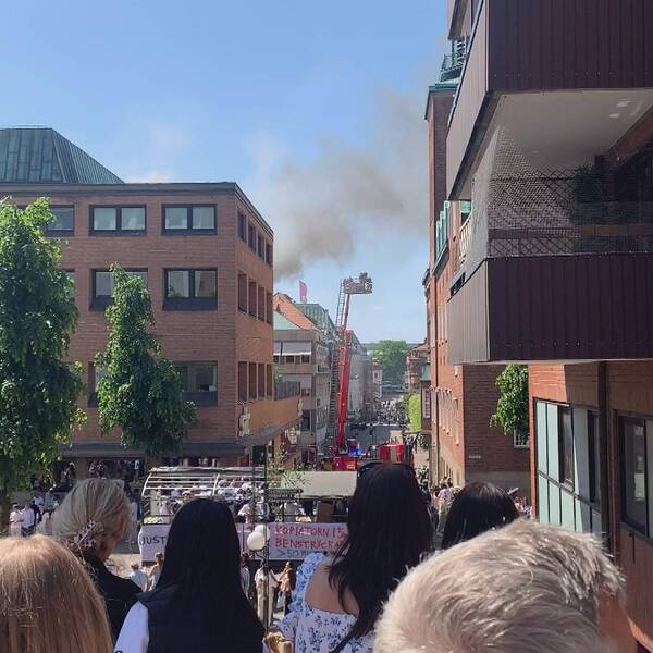Folksamling står och kollar på branden i ett lägenhetshus och studentflak passerar i bakgrunden.