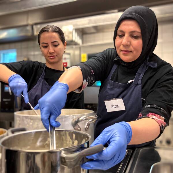 Två kvinnor står i ett kök på en folkhögskola i Göteborg. Framför sig har de stora kastruller som de rör om i.