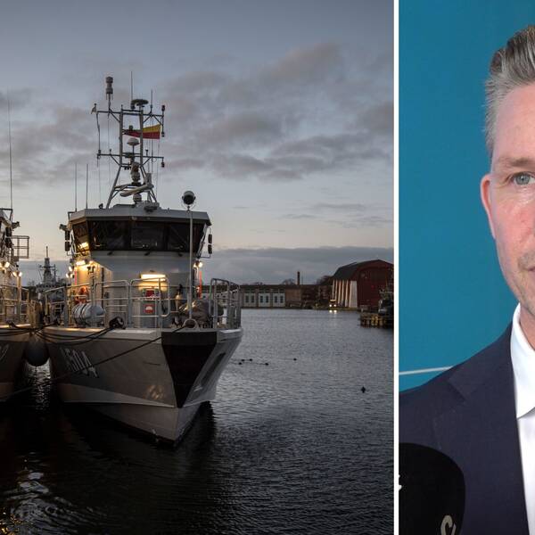 Till vänster två av försvarsmaktensbåtar i mörk hamn, Marinbasen Karlskrona. Till höger man med kort hår, vit skjorta och svart kavaj tittar snett till vänster i bild. Försvarsminister Pål Jonson, Moderaterna.