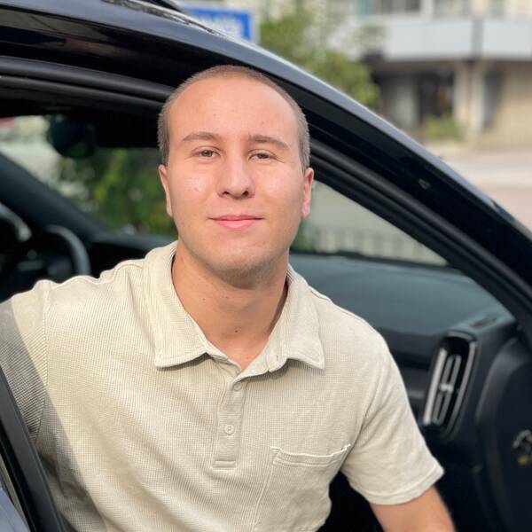 Man i beige pikétröja sitter i bil och tittar in i kameran. Julius Persson, trafiklärare Ronneby.