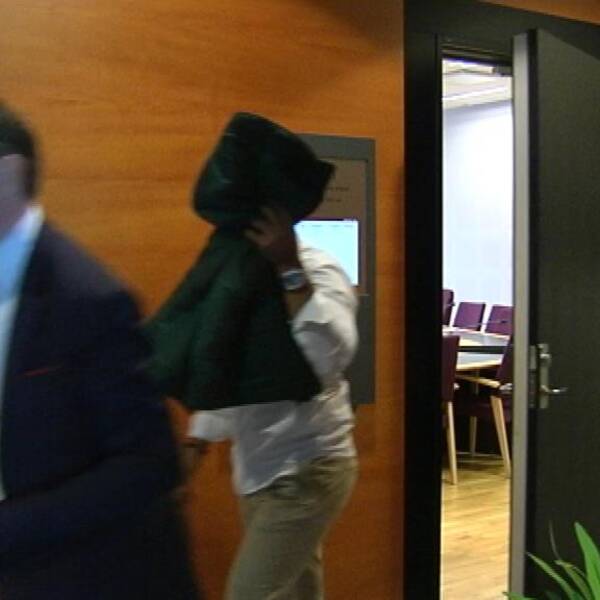 Den åtalade gothia cup-ledaren håller upp en jacka framför sitt ansikte