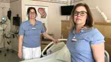 två kvinnor i sjukhuskläder vid patientsäng i sjukhusrum