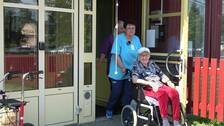 Olena Hrytsanchuk med en kollega och brukare – en gammal kvinna i rullstol – på väg ut på promenad. Olena är klädd i blått och har mörkt lockigt hår och hennes kollega har på sig lila kläder och långt ljust hår.
