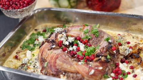 En ugnsform med en köttfärskrans med bacon runt om, toppad med persilja, fräska lingon och mögelost.