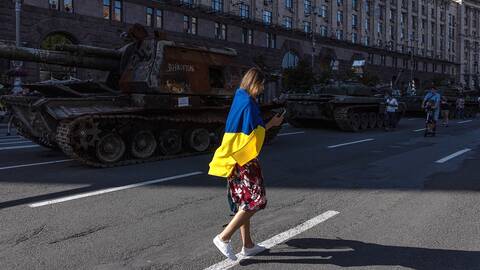 En kvinna med en ukrainsk flagga går förbi ryska militärfordon i Kiev. Bild från augusti 2022.