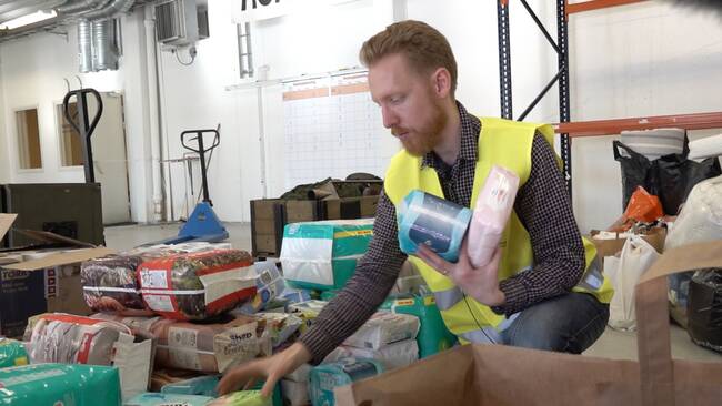 en man i skjorta och varselväst plockar paket med blöjor i en lagerlokal