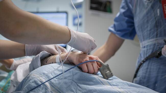 Person som ligger i sjukhussäng med monitor bakom. Man ser bara personens arm. Sjukvårdspersonal står bredvid och fäster slangar vid personens hand. Sverige har 21 regioner. De styr över sjukvården. Tidigare var det landstinget som hade hand om vården.