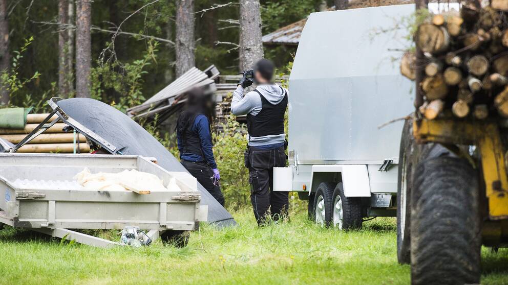 två poliser på en gård, släpvagnar och en traktor syns