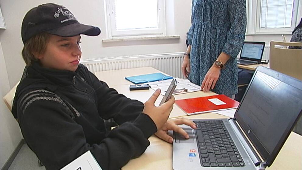 pojke med mobil och laptop i skolbänken