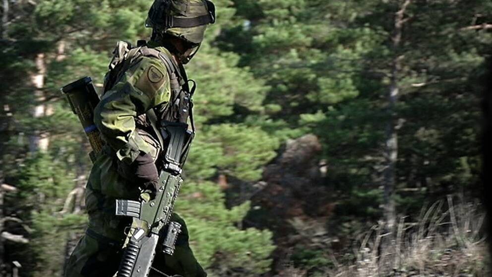 Soldat i uniform och vapen går i skog.