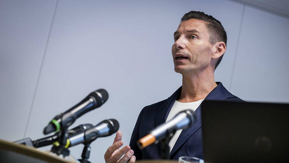 Elias står framför ett par mikrofoner på en presskonferens.