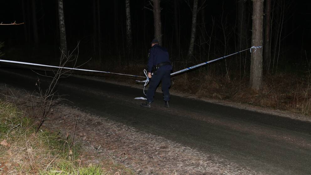 En polis som sätter upp ett avspärrningsband på en liten grusväg.