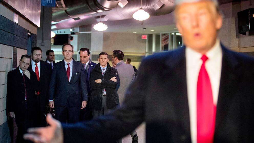 Donald Trump med några av hans närmaste män i bakgrunden, bland andra stabschefen Reince Priebus och säkerhetsrådgivaren Michael Flynn