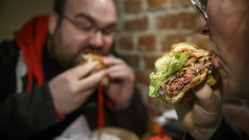 En bild på två personer som sätter i sig hamburgare.