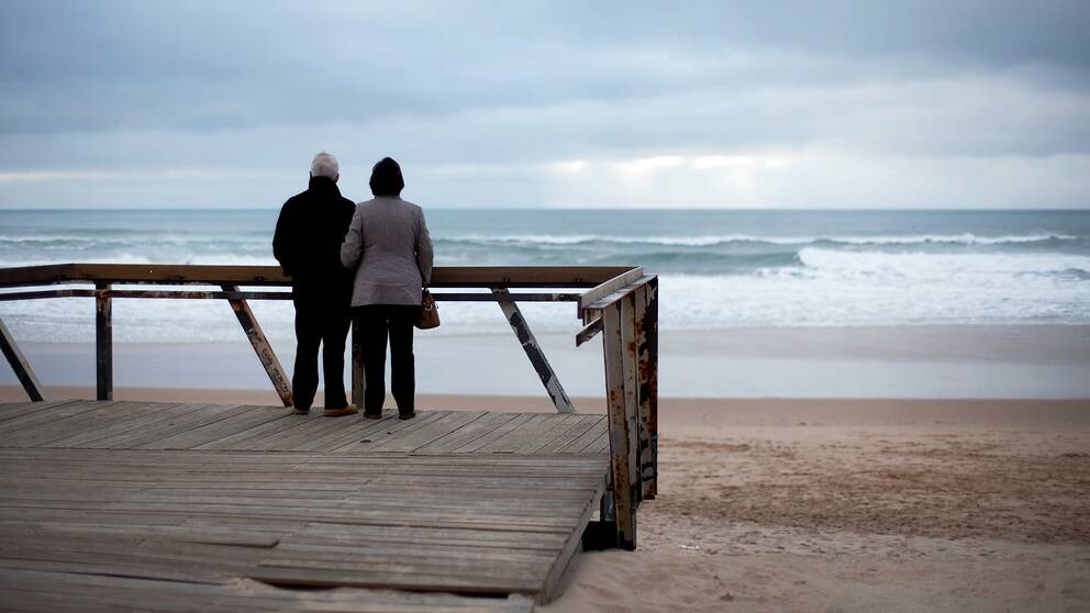 Äldre par som står på altan och blickar ut mot sandstrand och havet. Ska symbolisera pensionärer som bosatt sig i  Portugal som snart kan komma att behöva betala skatt i landet.