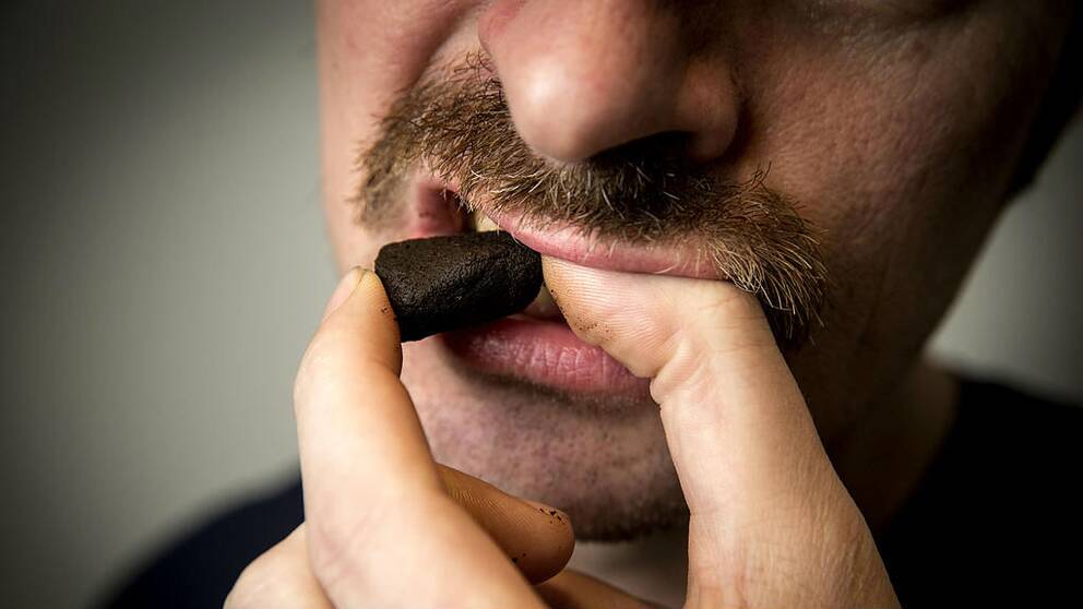 Närbild på en man med mustasch som lägger in en bakad snusprilla.