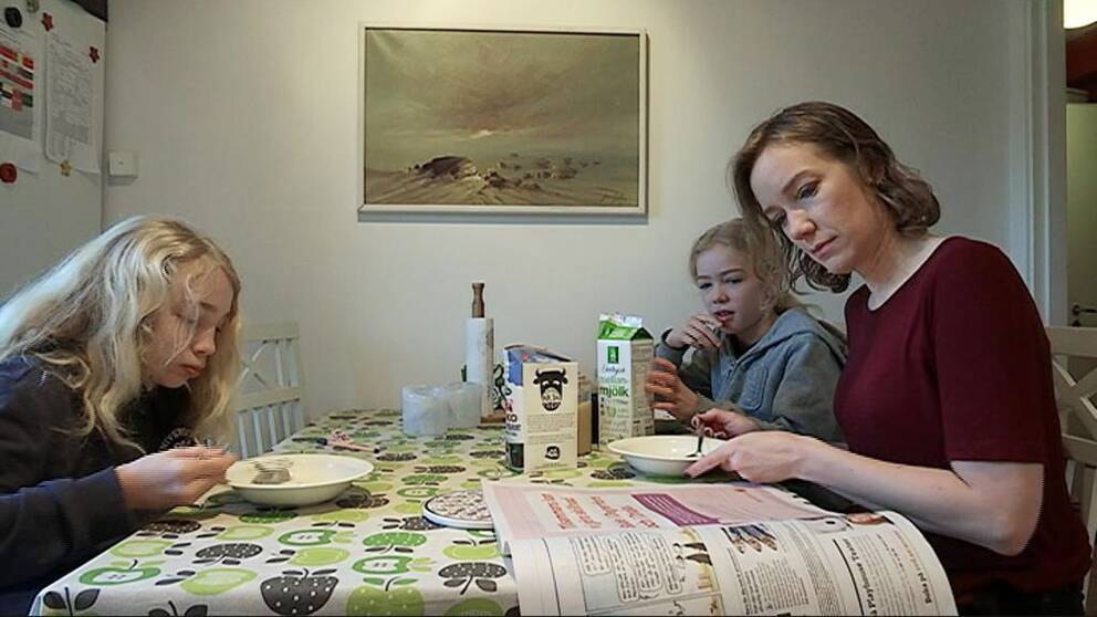Två barn äter frukost med sin mamma som läser tidningen och äter frukost.