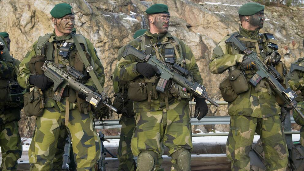 Tre beväpnade militärer med kamoflagemålning i ansiktet