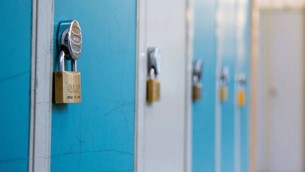 En elev går i en skolkorridor med blåa skåp