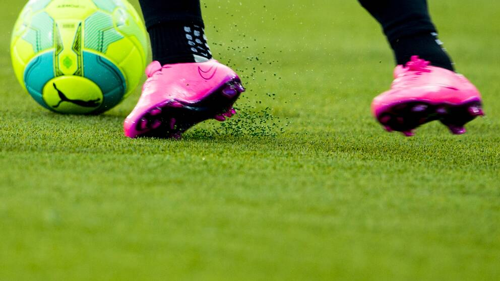 en fotboll och fötter i dobbade skor på konstgräs