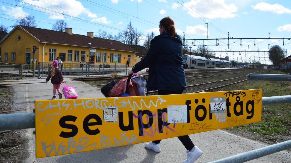 Familj passerar över spåret vid Södra station i Örebro. I förgrunden en skylt med texten ”se upp för tåg”.