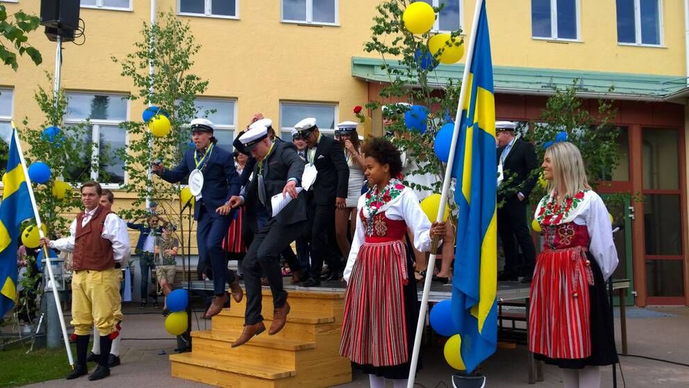 Ett gäng studenter står samlande med studentmössor på. Ballonger och Sverigeflaggor pryder scenen de står på.