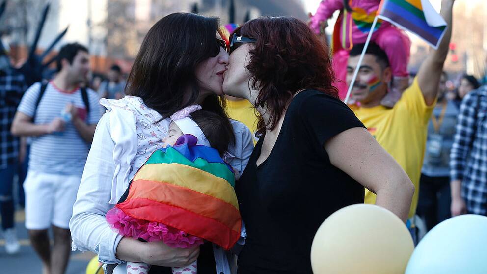 Två kvinnor kysser varandra i en prideparad.