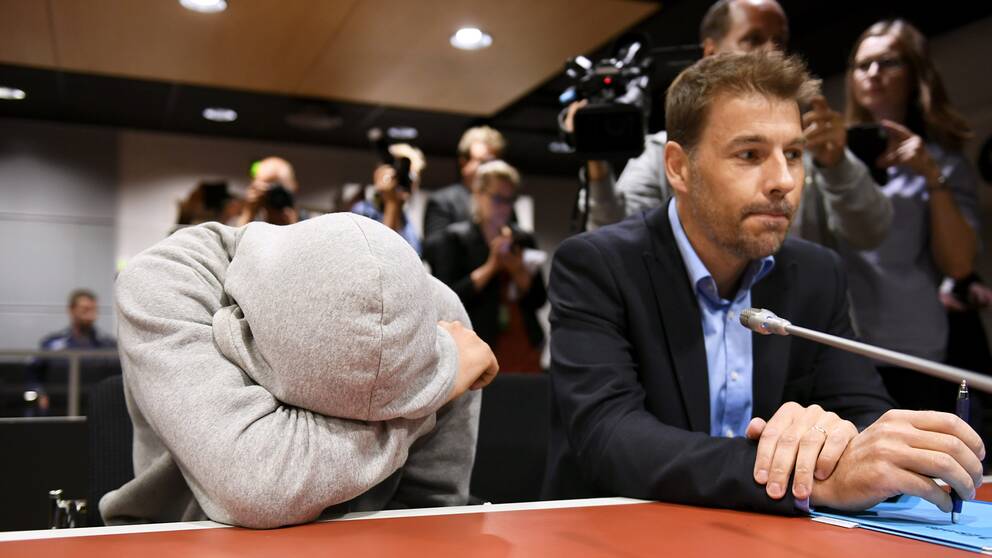 En av de misstänkta för inblandning i knivattacken i Åbo under häktningsförhandlingen. Han döljer sitt ansikte.