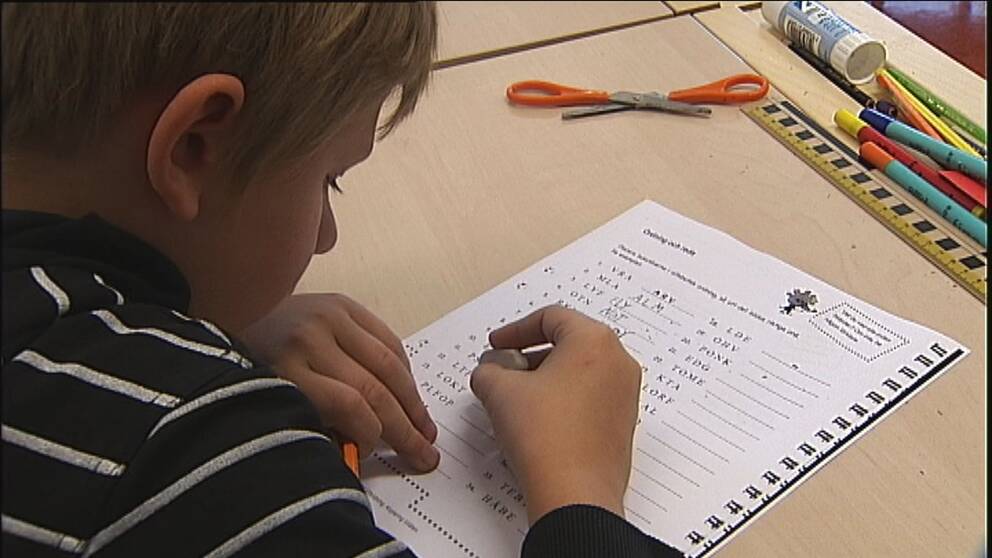 Pojke sitter vid en skolbänk och skriver