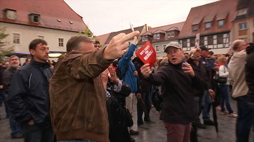 Flera personer på ett torg, en av dem pekar finger och andra är upprörda. Platsen är ett torg i Tyskland.