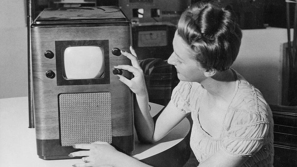 Svartvit bild av en kvinna som vrider på kanalratt på gammaldags tv.
