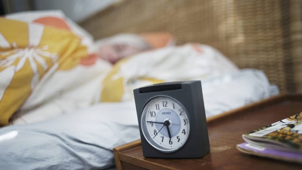 Kvinna sover med klocka i förgrunden