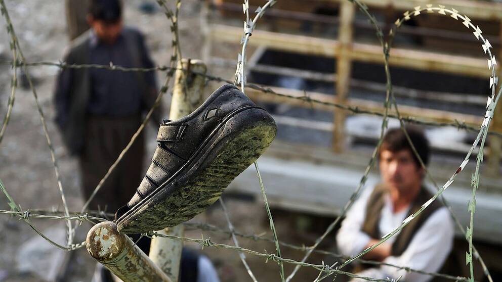 Afghan residents look at victim's footwear hanging on barbed wire outside the Imam Zaman Shiite mosque the day after a suicide attack during Friday evening prayers, in Kabul on October 21, 2017. A strong smell of blood and flesh permeated the Imam Zaman mosque in Kabul on October 21 hours after dozens of Shiite worshippers were slaughtered by a suicide bomber during evening prayers. Broken glass and dust covered the red carpet, soaked in the blood of the men, women and children who had been praying on Friday when the attacker blew himself up, causing carnage in the cavernous prayer hall. / AFP PHOTO / WAKIL KOHSAR