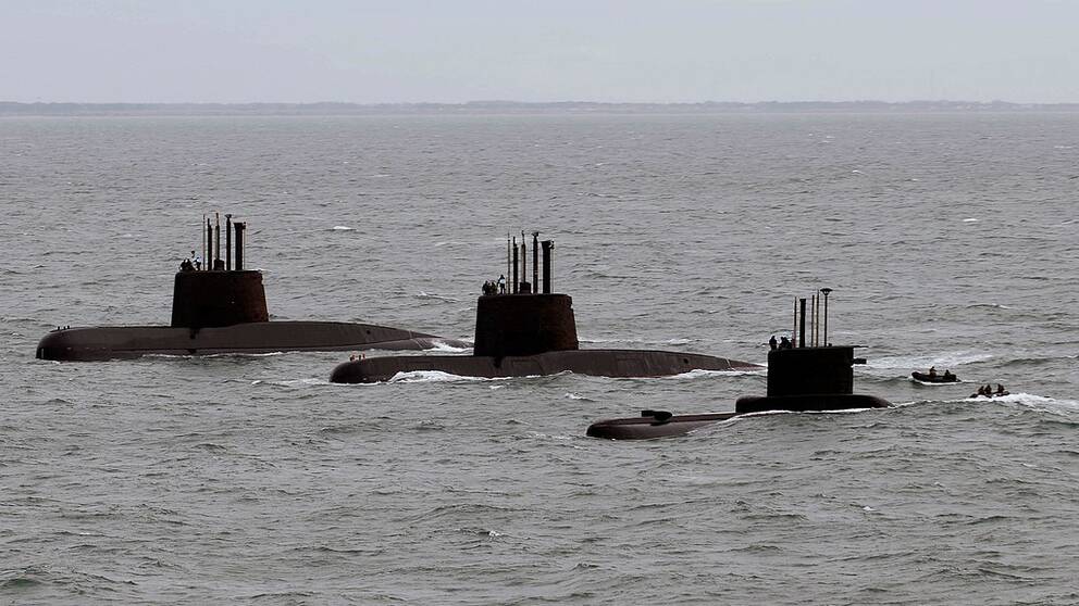 Tre ubåtar som stigit upp till ytan syns på rad i havet.