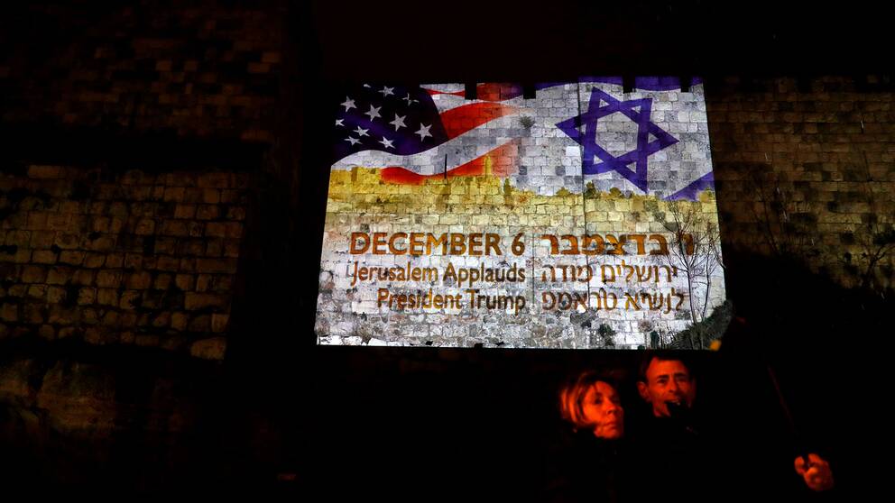 Två personer i Jerusalem framför en projektion med USA:s och Israels flaggor