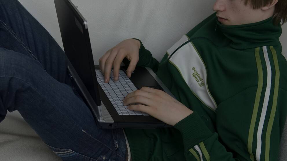 En pojke sitter med en bärbar dator i knät i en soffa.