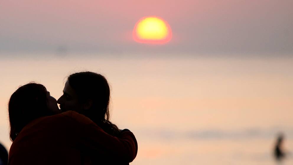Siluetter av par som kysser varandra med solnedgång i bakgrunden.