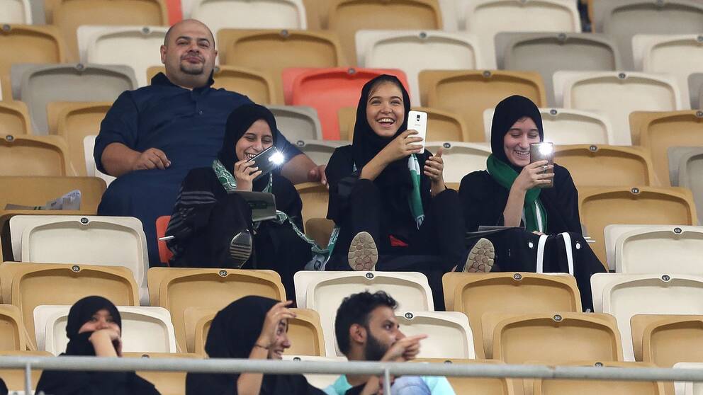 En familj med tre kvinnor och en man sitter på läktaren vid en fotbollsmatch i Saudiarabien.