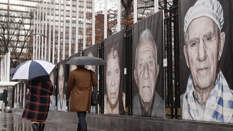 Umbrella-toting pedestrians pass Luigi Toscano's larger-than-life sized photographic portraits of Holocaust survivors, Tuesday, Jan. 23, 2018, outside United Nations headquarters in New York. Toscano's pictures are part of a two-part exhibit at the UN entitled ”Survivors, Victims and Perpetrators,” in conjunction with the Lest We Forget project, commemorating Holocaust victims and survivors. The UN exhibition has two parts: one section focuses on the 1942 Wannsee Conference, its participants and Nazi persecution policies leading to deportations of European Jews and their subsequent murder. The other part features Toscano's portraits of Holocaust survivors living in Germany, the United States, Ukraine, Israel and Russia, sharing their personal stories. (AP Photo/Kathy Willens)