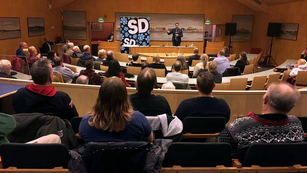 Svergiedemokraternas partiledare Jimmie Åkesson står framför människor i en sal.