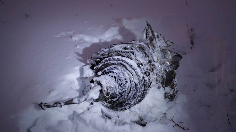Närbild på en vrakdel av det kraschade planet, på en snöig äng.