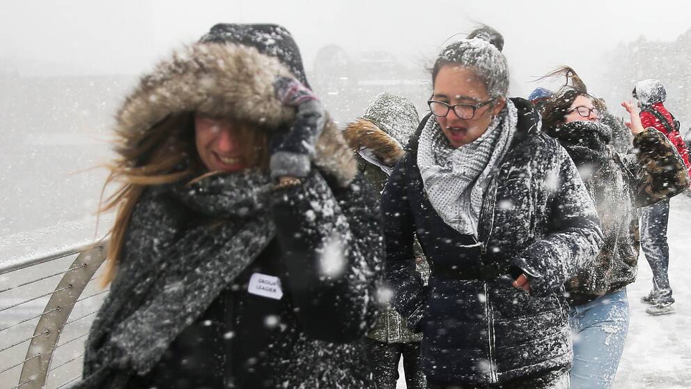 Fotgängare korsar Millennium Bridge över Themsen i London, som drabbats av kraftigt snöfall.