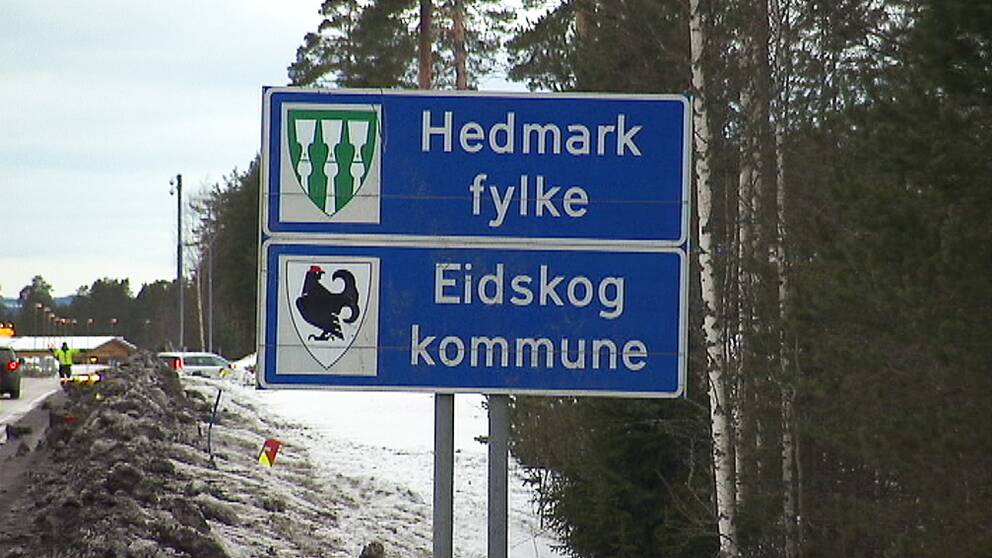 Två vägskyltar på varandra. På den ena står det ”Hedmark fylke” och på den andra står det ”Eidskog kommune”