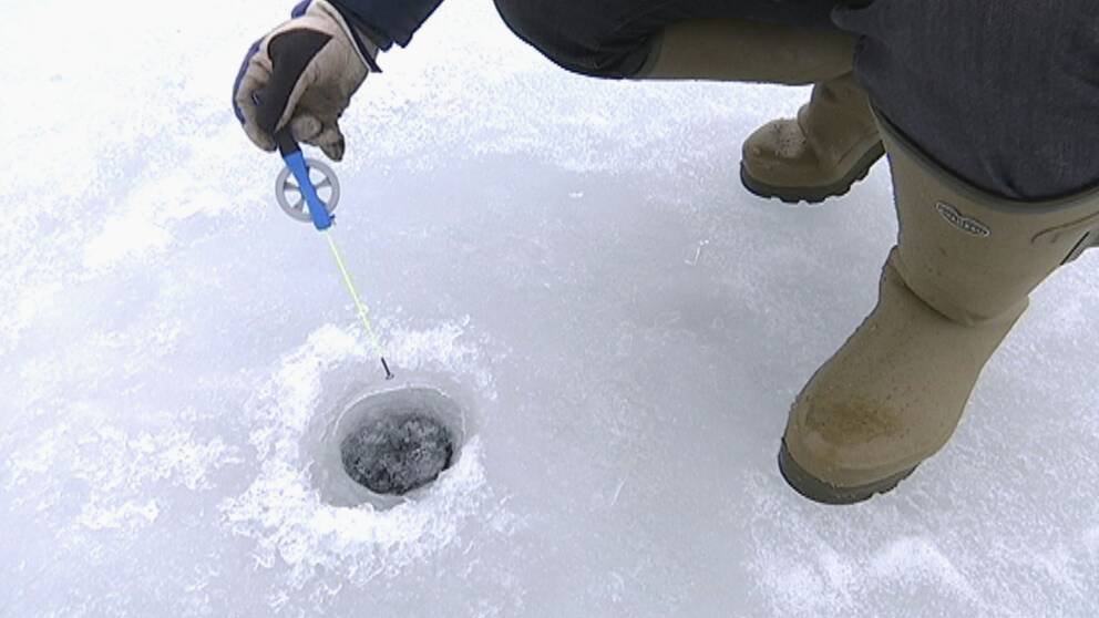foto neråt som visar hand som håller pimpelspö ner mot ett hål i isen, och fötterna på person