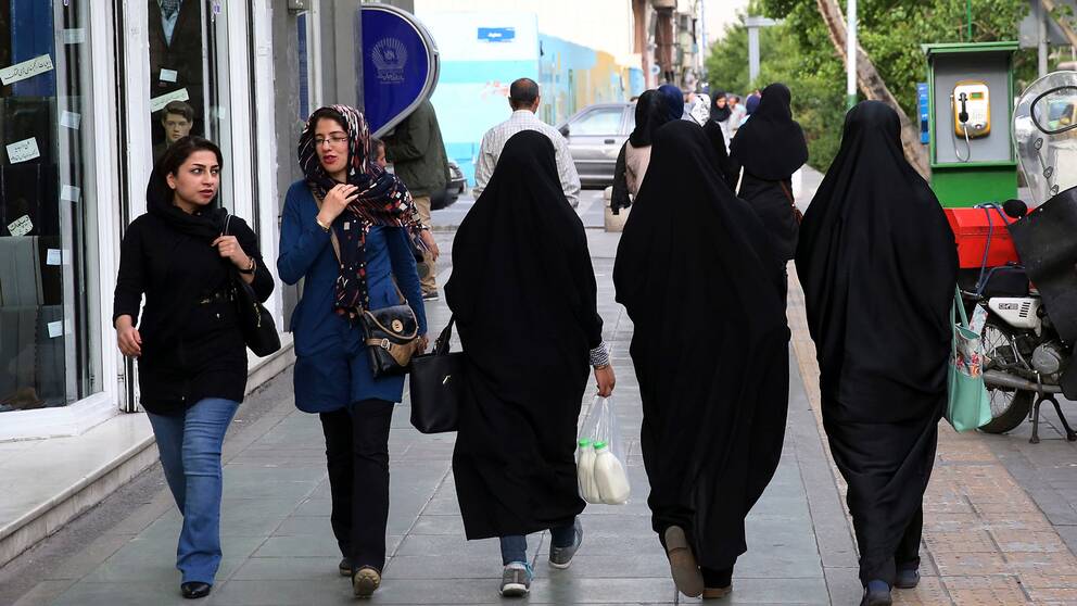 Fem kvinnor går på gatan i Teheran, Iran. Två har slöja, tre har den traditionella chadoren.
