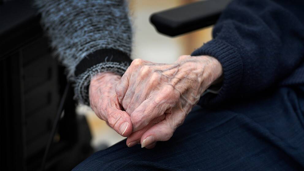 Två personer håller varandra i hand på ett äldreboende.