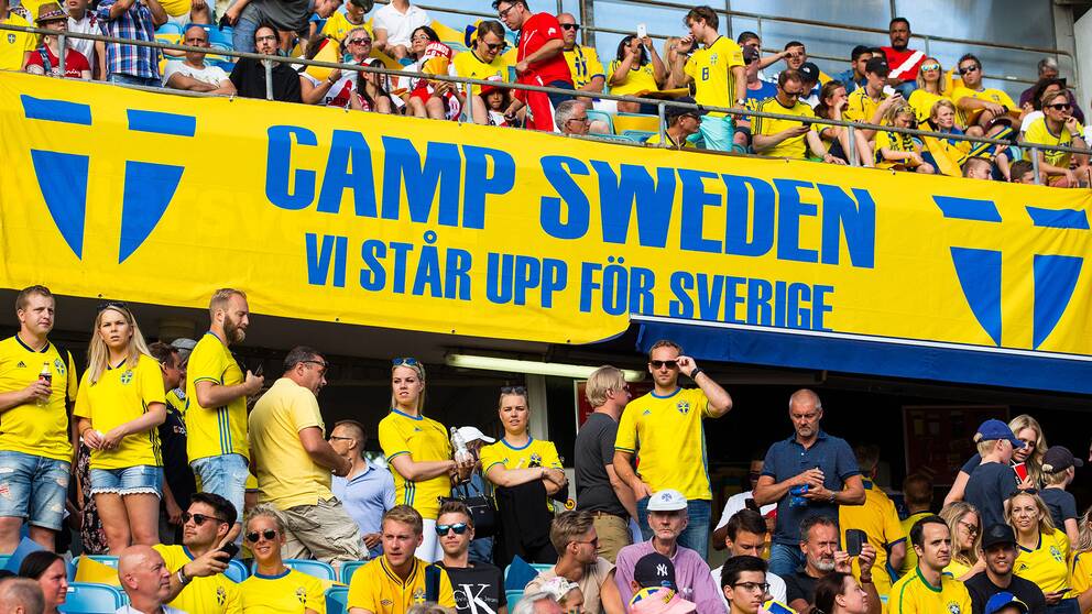 Fullt med fans klädda i svenska gulblå matchtröjor på en fotbollsläktare.